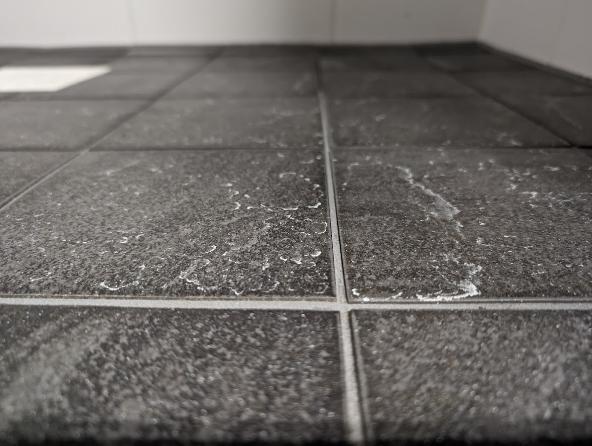 Achtergebleven minerale aanslag op een tegelvloer in een badkamer.